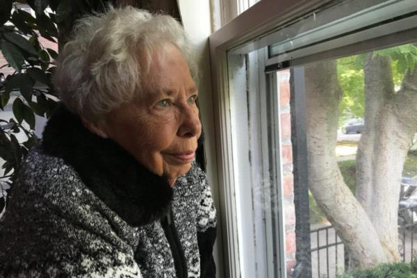 Elderly woman gazes out the window of her home.